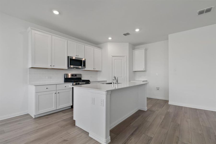 Kitchen with a kitchen island with sink, stainless steel appliances, light hardwood / wood-style floors, and white cabinetry