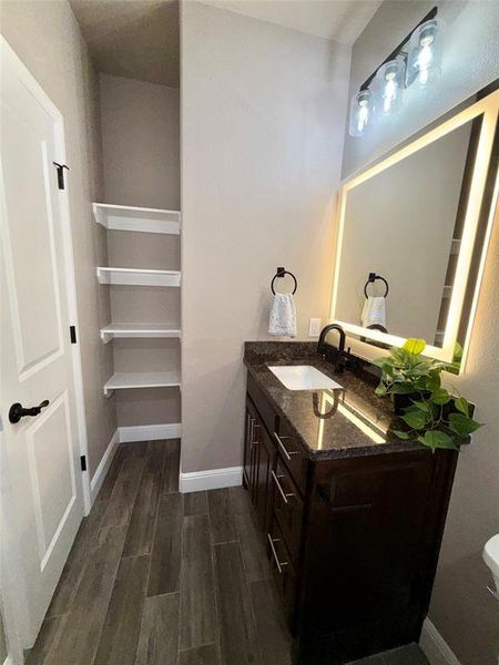 Bathroom featuring a dark wood vanity with a granite countertop, undermount sink, and black faucet. Hidden linen shelves for storage