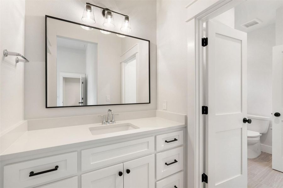A well-appointed bathroom features a single vanity with stone counters and an expansive mirror.