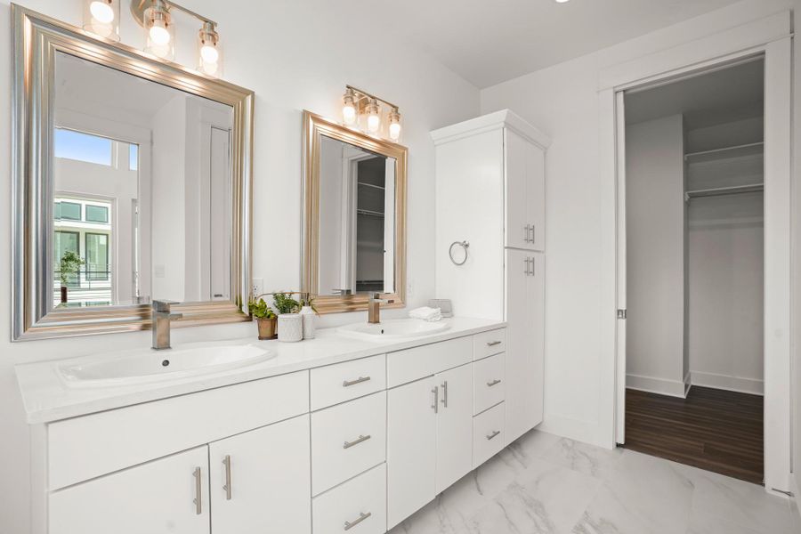 Dual vanities and a built-in storage cabinet complement this well-lit primary bathroom. Dual vanities and a built-in storage cabinet complement this well-lit primary bathroom.
