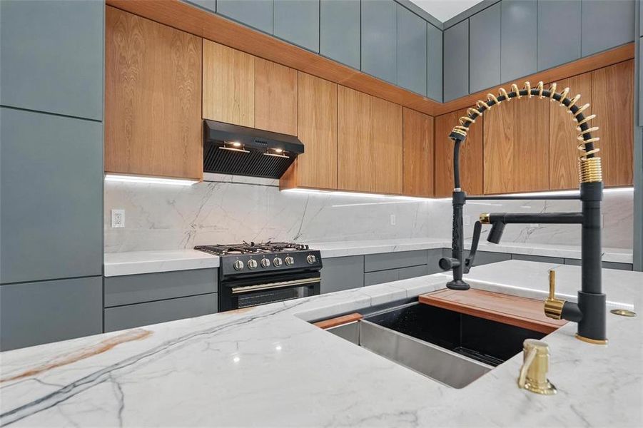 Kitchen with backsplash, extractor fan, light stone countertops, gas stove, and modern cabinets Kitchen with backsplash, extractor fan, light stone countertops, gas stove, and modern cabinets