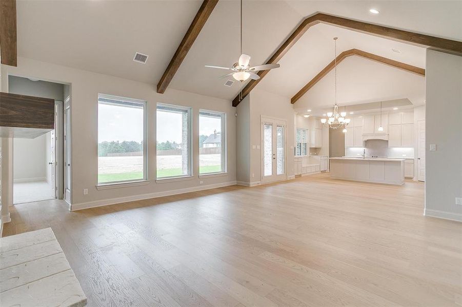 Unfurnished living room featuring beamed ceiling, light hardwood / wood-style flooring, ceiling fan with notable chandelier, and high vaulted ceiling