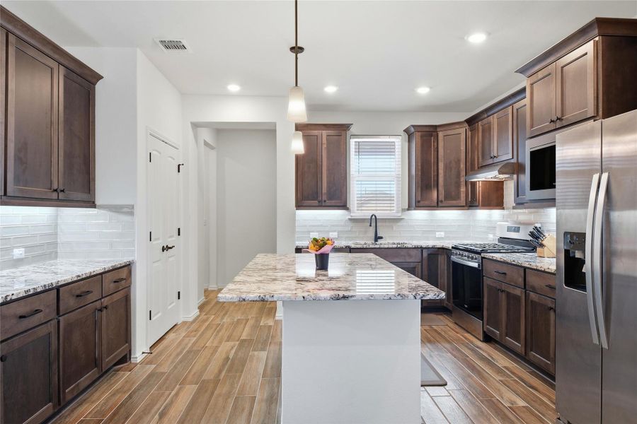 Kitchen featuring stainless steel appliances, light stone countertops, a kitchen island, wood tiled floors, and pendant lighting