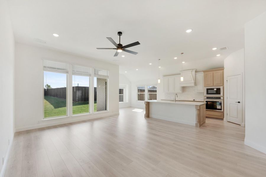 Open-concept living area with light wood floors, ceiling fan, and kitchen island with white cabinets and stainless appliances.