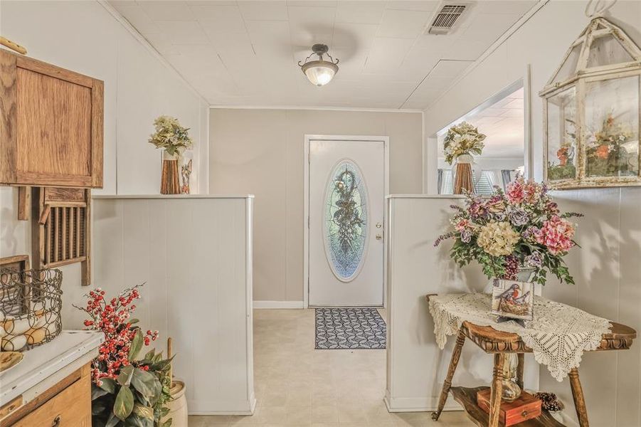 Entryway featuring a white door with an oval stained-glass insert, light-colored flooring, and light wall paneling Entryway featuring a white door with an oval stained-glass insert, light-colored flooring, and light wall paneling
