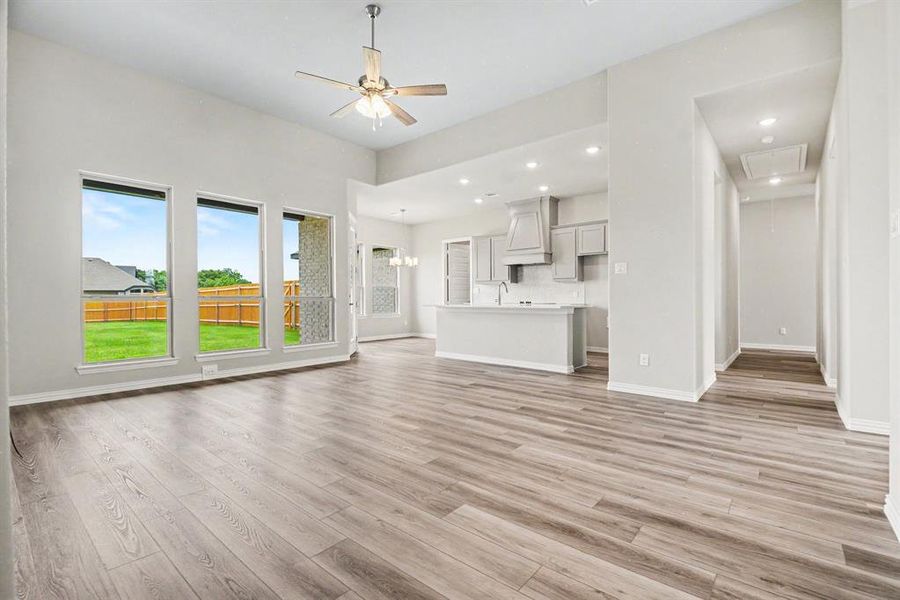 Spacious living area featuring high ceilings, wood-finish flooring, and multiple large windows overlooking a fenced backyard Spacious living area featuring high ceilings, wood-finish flooring, and multiple large windows overlooking a fenced backyard
