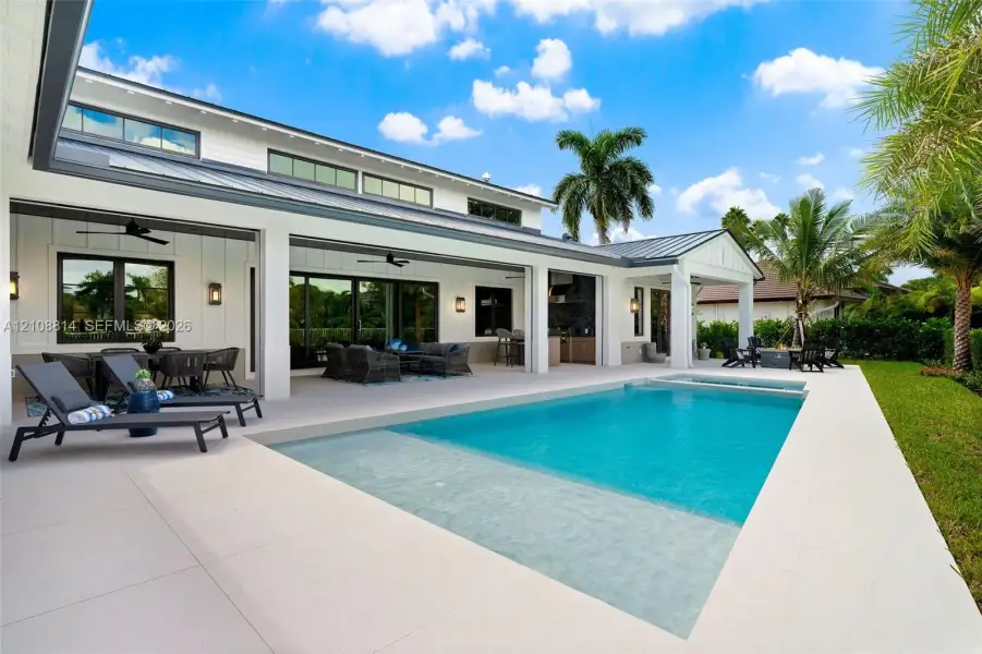 Covered lanai with recessed lighting, in-ground pool featuring a sun shelf, integrated spa, and vertical board-and-batten siding Covered lanai with recessed lighting, in-ground pool featuring a sun shelf, integrated spa, and vertical board-and-batten siding