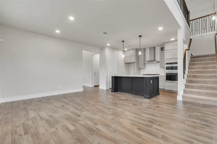 A well-lit, open-concept living area with a contemporary kitchen and a carpeted staircase leading to the upper level.