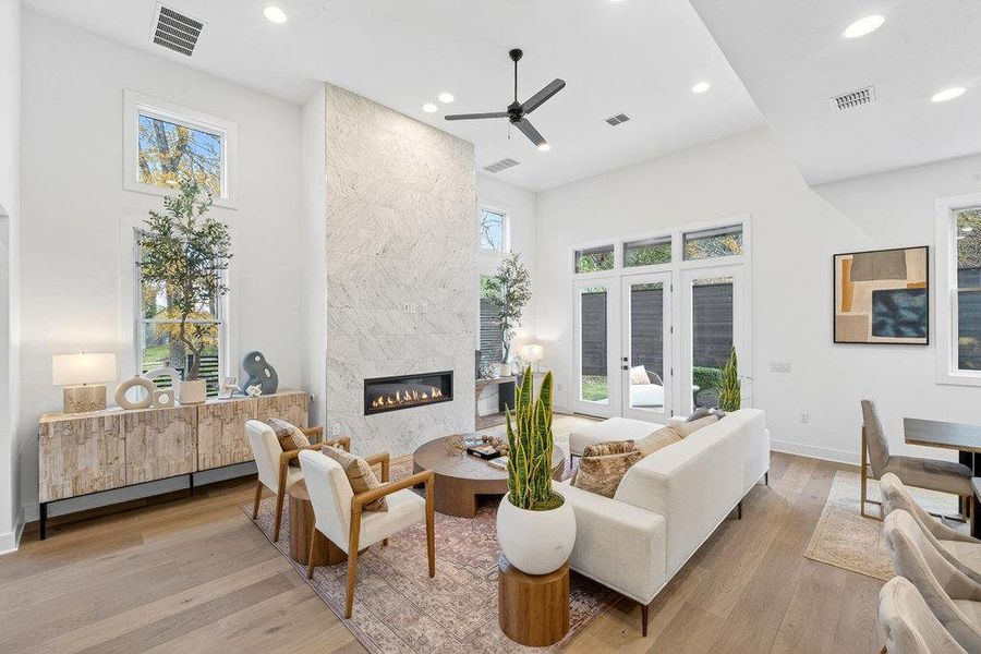 Living room featuring a high end fireplace, hardwood / wood-style flooring, recessed lighting, a ceiling fan, and a towering ceiling