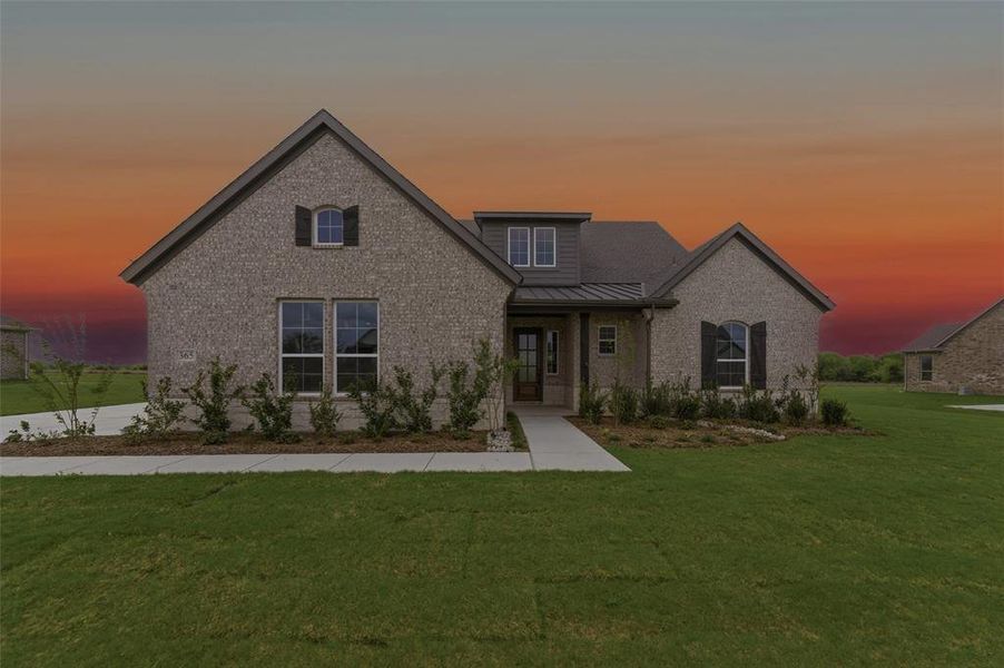 View of front of home featuring a front lawn, brick siding, covered porch, and a metal roof