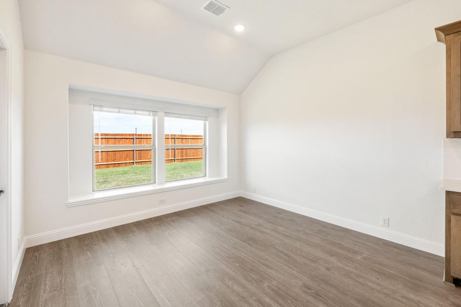 Empty room with vaulted ceiling, hardwood floors, and double window overlooking fenced backyard