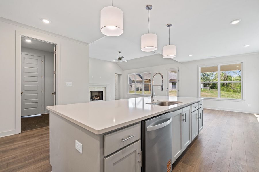 Kitchen featuring decorative light fixtures, a fireplace, an island with sink, stainless steel dishwasher, and vaulted ceiling