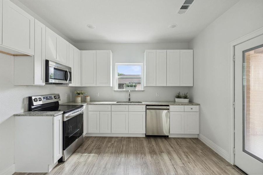 Kitchen with appliances with stainless steel finishes, sink, white cabinets, and light hardwood / wood-style floors