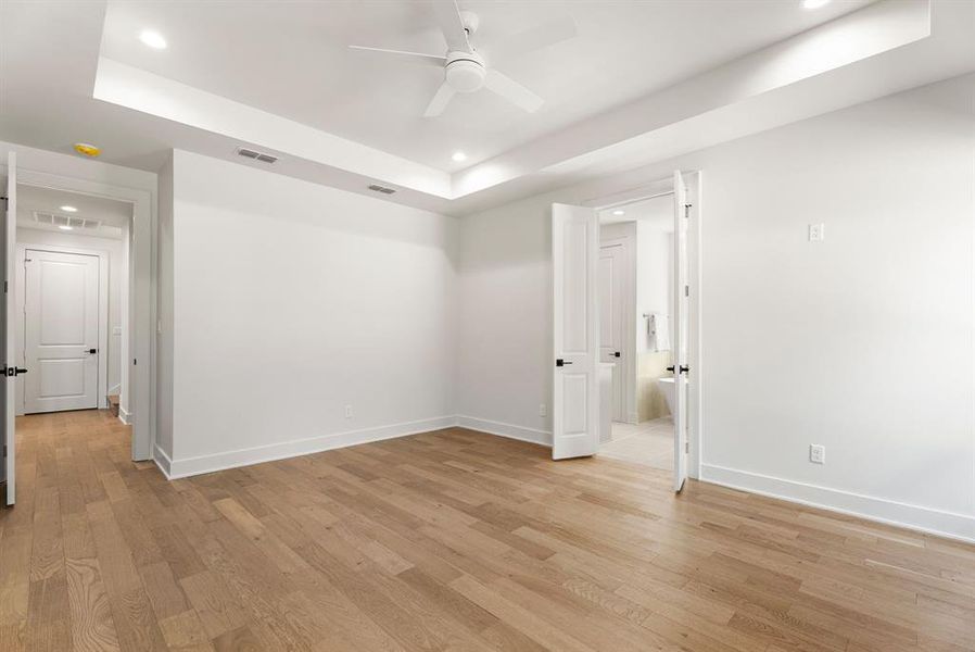 Empty room featuring a tray ceiling, recessed lighting, light wood-style flooring, and a ceiling fan