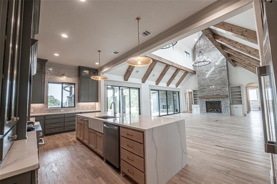 Kitchen with light stone countertops, light wood-type flooring, decorative light fixtures, high vaulted ceiling, and beam ceiling Kitchen with light stone countertops, light wood-type flooring, decorative light fixtures, high vaulted ceiling, and beam ceiling