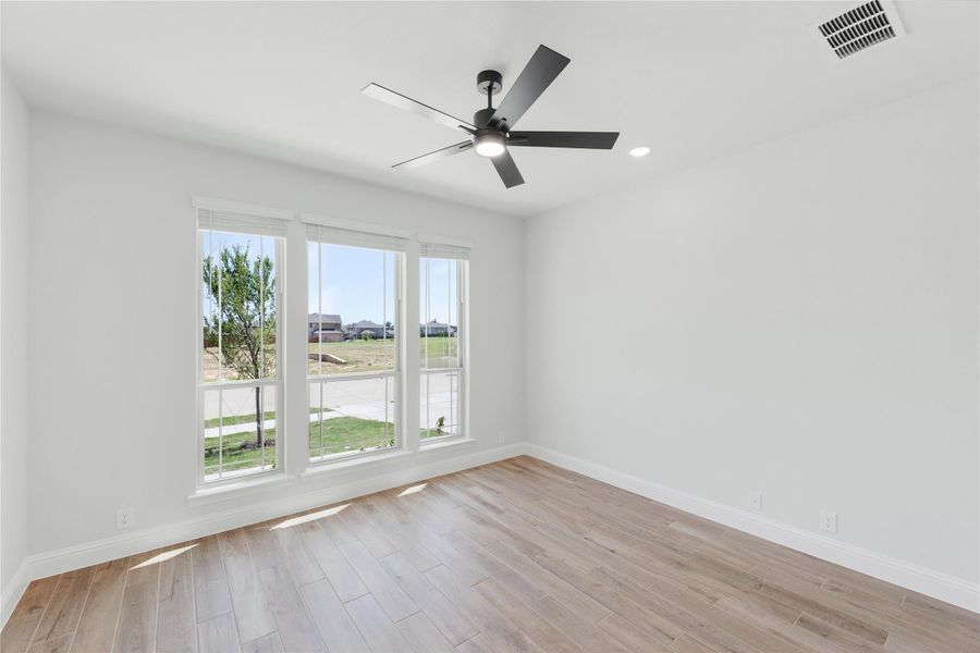 Empty room with light wood floors, white walls, ceiling fan, and three windows with outdoor views Empty room with light wood floors, white walls, ceiling fan, and three windows with outdoor views