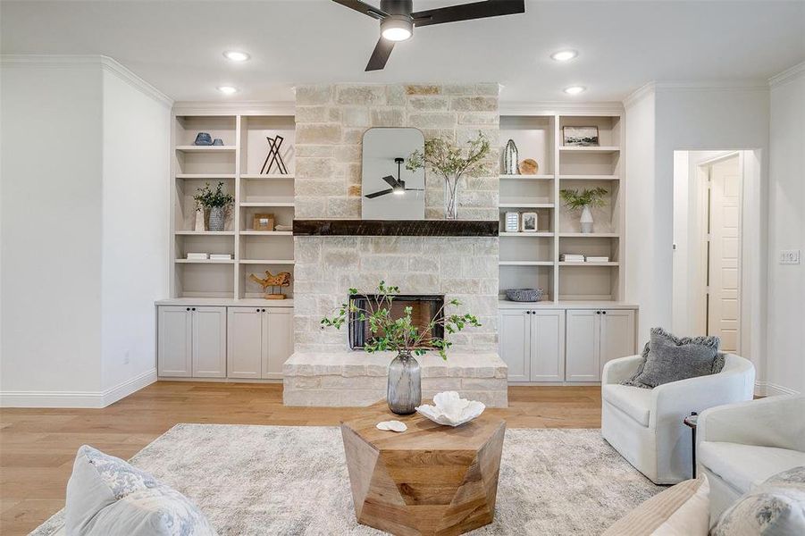 Living room with a stone fireplace, light hardwood / wood-style flooring, ornamental molding, and ceiling fan