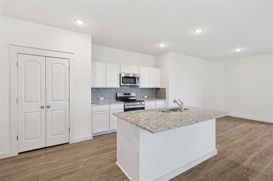 Kitchen featuring light hardwood / wood-style floors, sink, an island with sink, white cabinetry, and appliances with stainless steel finishes