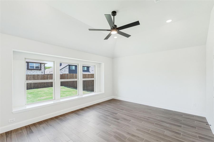 Empty room with wood-look tile floors, black ceiling fan, and triple windows overlooking a fenced backyard Empty room with wood-look tile floors, black ceiling fan, and triple windows overlooking a fenced backyard