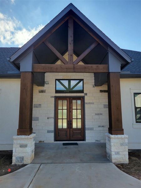Charming entrance featuring a covered porch with a peaked roof supported by sturdy wooden beams. The front door is elegant, with glass panels, set in a stone facade that adds character and warmth. Charming entrance featuring a covered porch with a peaked roof supported by sturdy wooden beams. The front door is elegant, with glass panels, set in a stone facade that adds character and warmth.