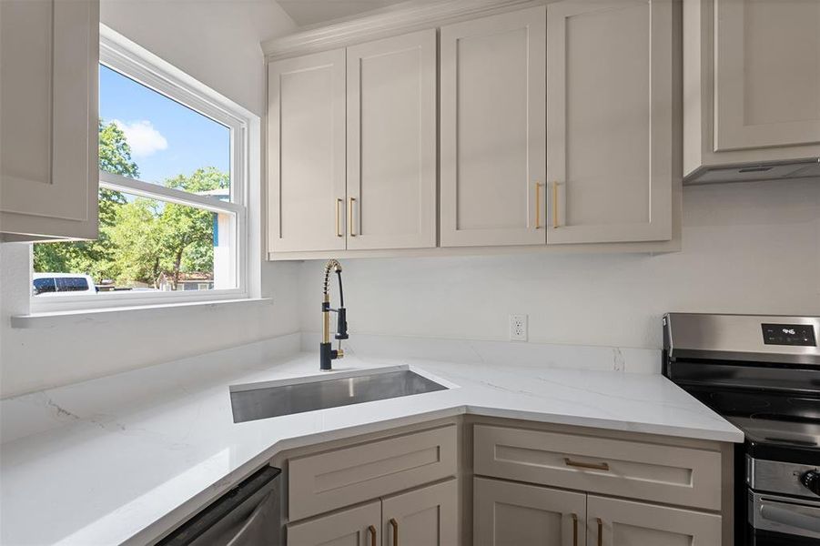 Well-appointed kitchen featuring light-toned cabinetry with brass hardware, quartz countertops, and a modern gooseneck faucet