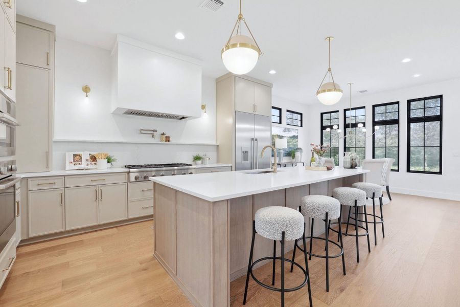 Two tone kitchen with two tone color scheme, pendant lighting, light wood-style flooring, a kitchen breakfast bar, and an island with sink