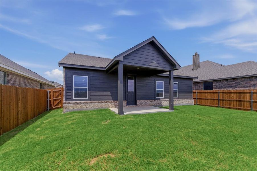 Spacious rear yard with a covered patio, dark siding, and a partial stone facade