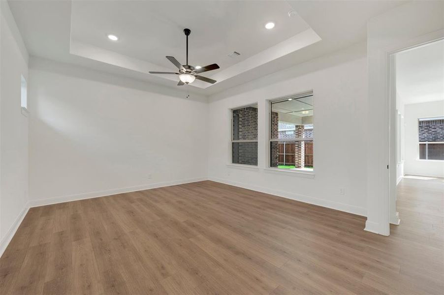 Spacious room featuring wood-finish flooring, a tray ceiling, recessed lighting, and a ceiling fan Spacious room featuring wood-finish flooring, a tray ceiling, recessed lighting, and a ceiling fan