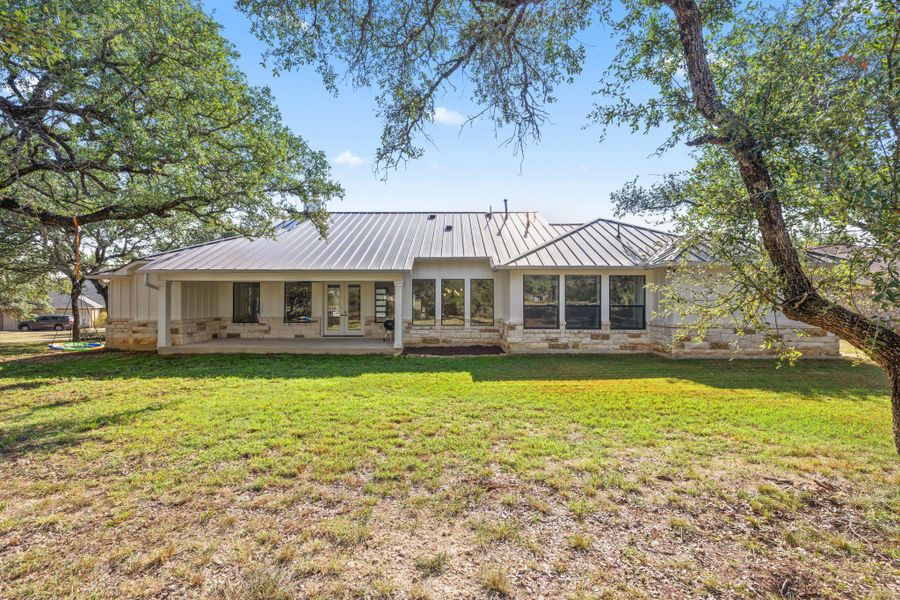 Back of house featuring a yard, a patio area, board and batten siding, stone siding, and a metal roof