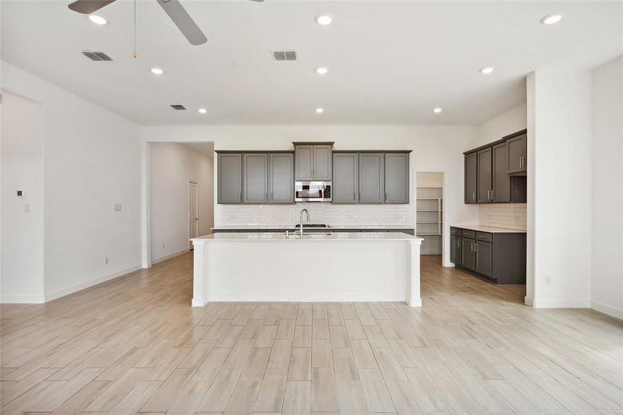 Kitchen with decorative backsplash, ceiling fan, a kitchen island with sink, light hardwood / wood-style floors, and sink