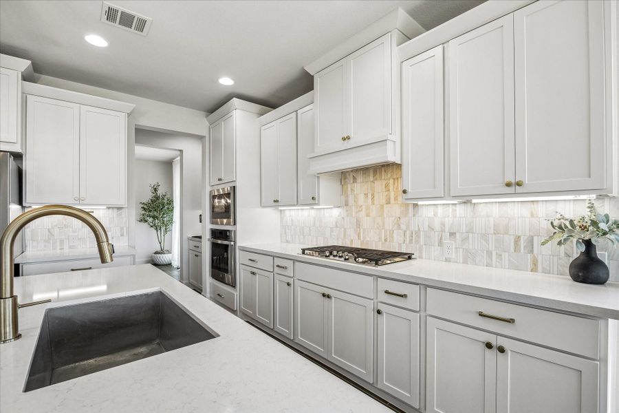 Gourmet kitchen features custom cabinetry, quartz countertops, under-cabinet lighting and a designer tile backsplash