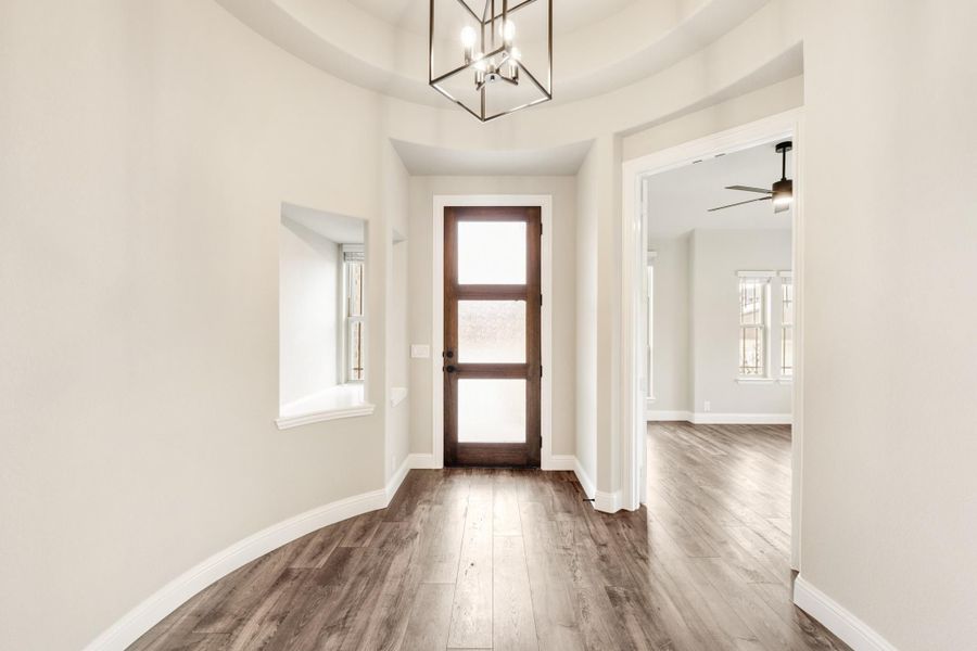 Entryway with wood floors, glass-panel front door, and metal chandelier overhead Entryway with wood floors, glass-panel front door, and metal chandelier overhead