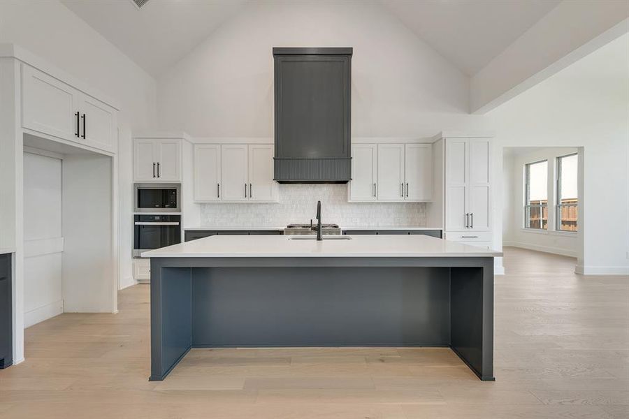 Kitchen with white cabinetry, light wood-type flooring, high vaulted ceiling, appliances with stainless steel finishes, and an island with sink Kitchen with white cabinetry, light wood-type flooring, high vaulted ceiling, appliances with stainless steel finishes, and an island with sink
