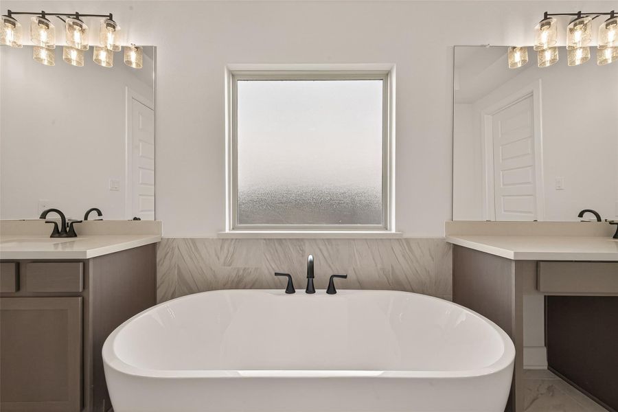 This bathroom features a modern design with a central freestanding bathtub, dual sinks with sleek black fixtures, and elegant lighting. A large frosted window provides privacy while allowing natural light to fill the space.