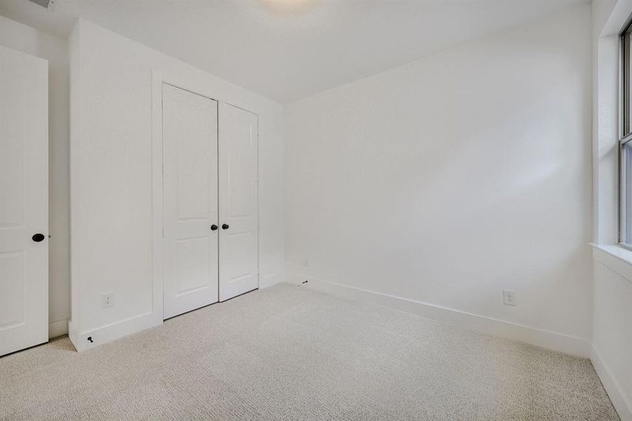 Bright interior room featuring light-toned carpeting, white walls, and a window with natural light