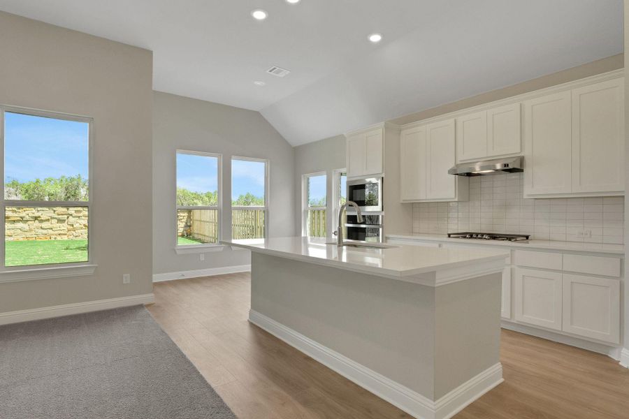 Kitchen featuring lofted ceiling, an island with sink, gas cooktop, under cabinet range hood, and decorative backsplash