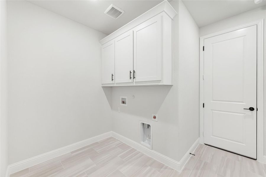 Laundry room with white upper cabinets, washer and dryer hookups, and light tile flooring Laundry room with white upper cabinets, washer and dryer hookups, and light tile flooring