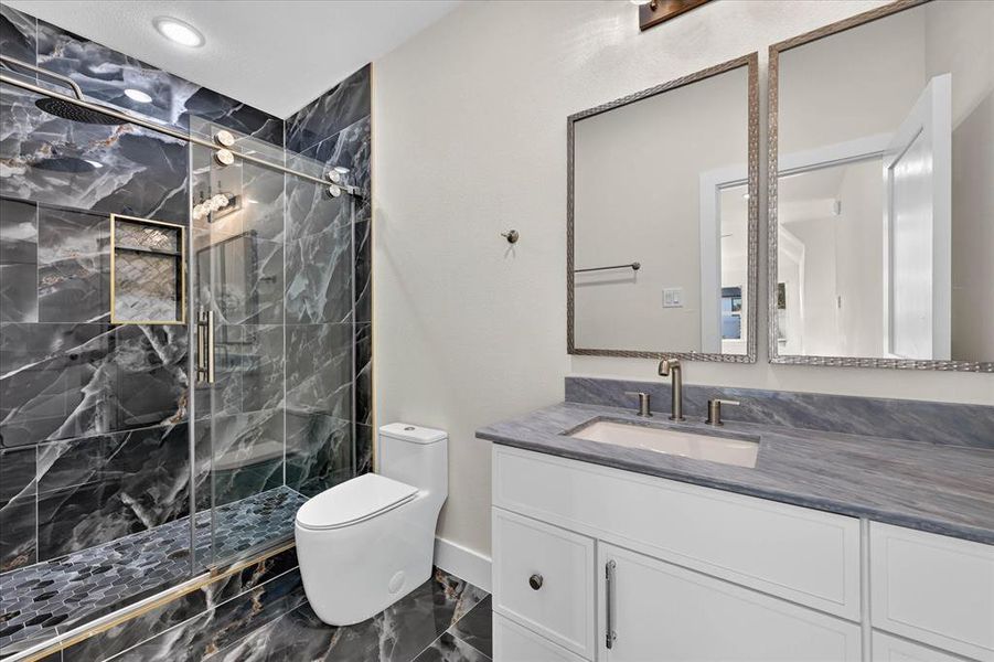 Bathroom featuring a spacious walk-in shower with dark marbled tile, a glass sliding door, and a built-in shower niche Bathroom featuring a spacious walk-in shower with dark marbled tile, a glass sliding door, and a built-in shower niche