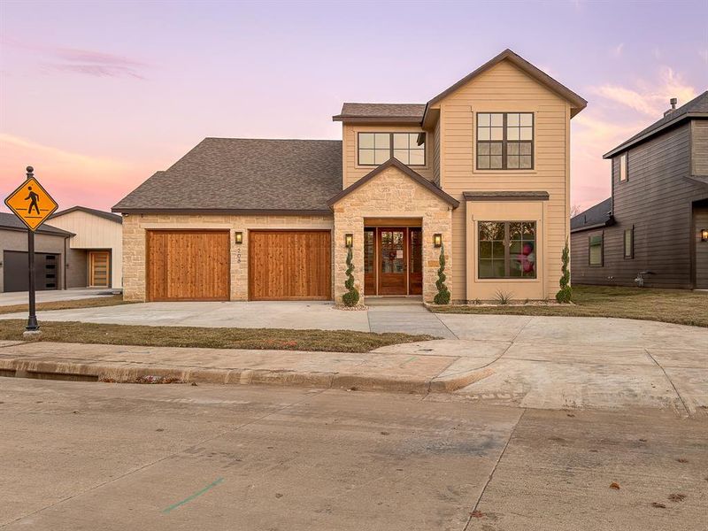 Contemporary facade featuring a stone and siding exterior, a two-car wood-finish garage, a stone archway entry, and dark framed windows