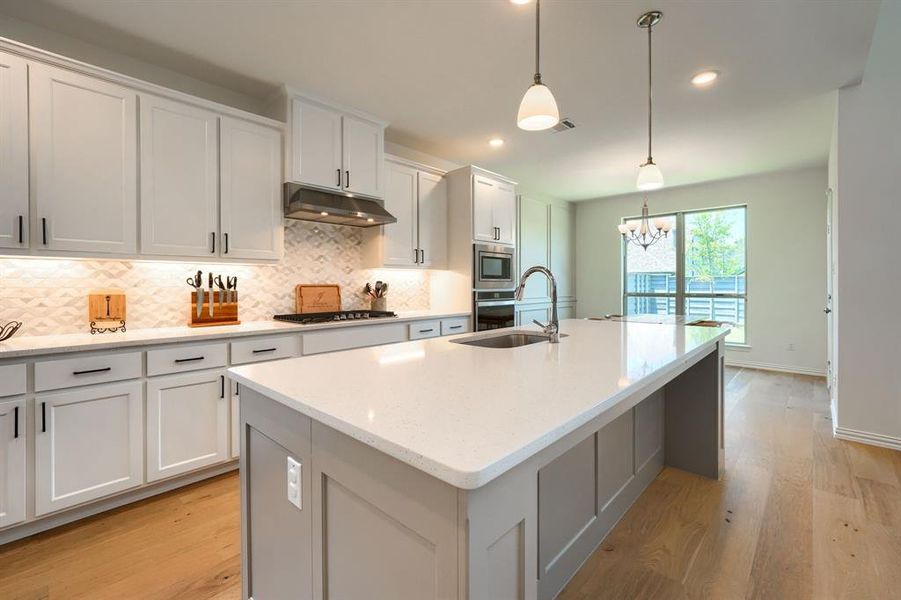 Kitchen featuring backsplash, an island with sink, light hardwood / wood-style flooring, and decorative light fixtures