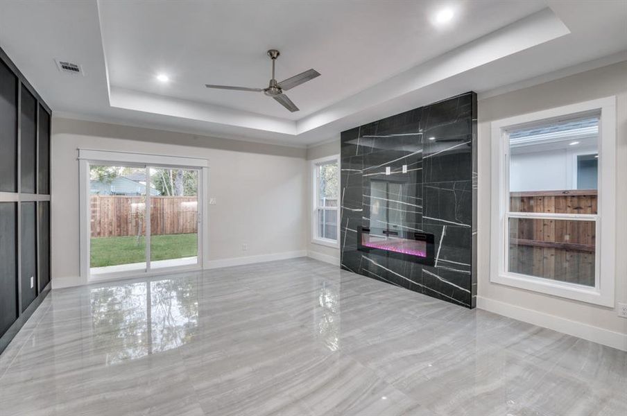 Unfurnished living room featuring a fireplace, a tray ceiling, and ceiling fan