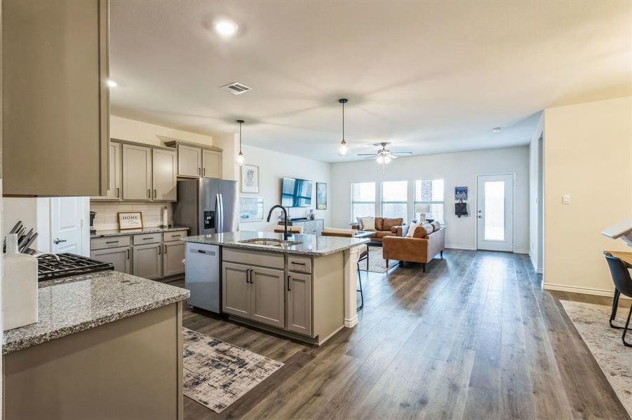 Kitchen with gray cabinets, pendant lighting, sink, appliances with stainless steel finishes, and an island with sink