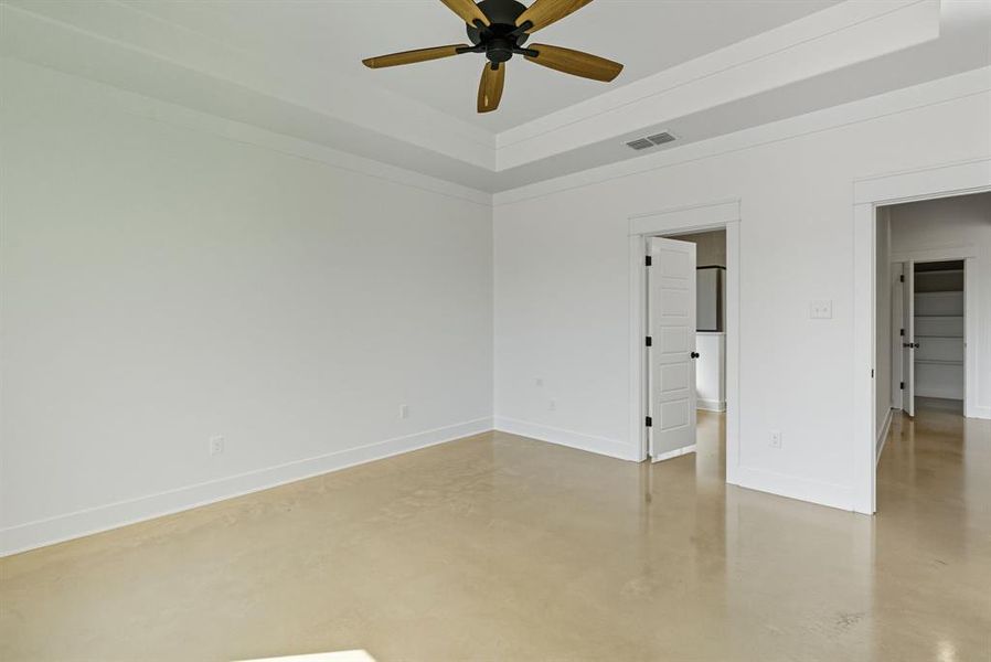 Unfurnished bedroom with concrete flooring, a raised ceiling, and ceiling fan