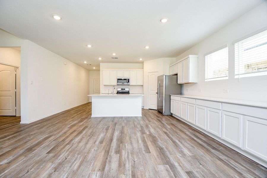 This modern kitchen features an open layout with sleek white cabinetry, stainless steel appliances, and ample natural light. The spacious island and wood-style flooring add to its appeal, making it ideal for both cooking and entertaining.