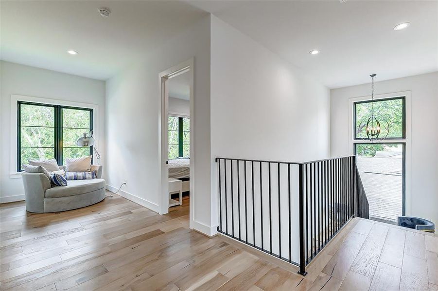 A cozy seating or reading area by the window with a plush swivel accent barrel chair, and an elegant light fixture. The space opens to two of the bedrooms, creating a welcoming and connected feel.