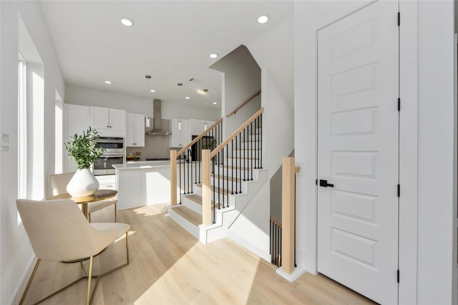 A bright and sophisticated open-concept space featuring a modern staircase, light wood flooring, and a sleek white kitchen that creates an airy and elegant flow throughout the home.