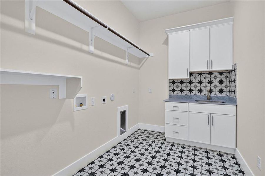 Laundry room featuring patterned floor tile, white shaker cabinetry, a utility sink with a brushed metal faucet, a dark countertop, and open shelving with a hanging rod Laundry room featuring patterned floor tile, white shaker cabinetry, a utility sink with a brushed metal faucet, a dark countertop, and open shelving with a hanging rod