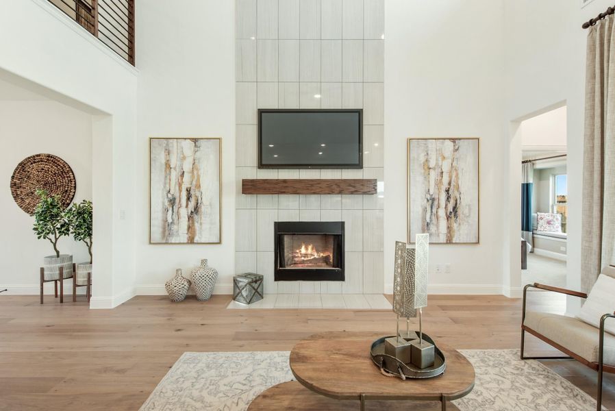 Living room with two-story tiled fireplace, wall-mounted TV, wood mantel, and hardwood floors Living room with two-story tiled fireplace, wall-mounted TV, wood mantel, and hardwood floors