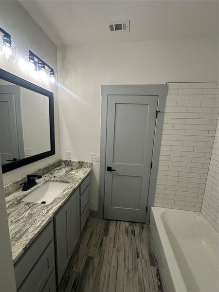 Full bath featuring vanity, a tub to relax in, and dark wood-type flooring
