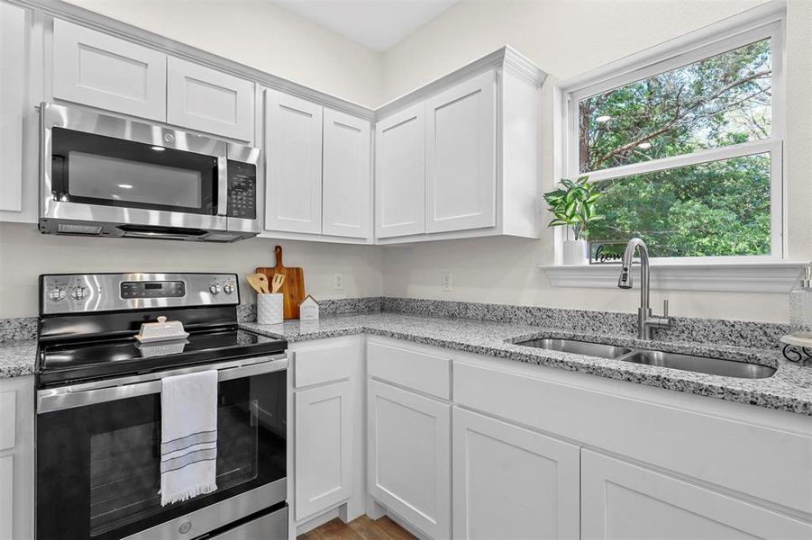 Kitchen with light stone counters, hardwood / wood-style flooring, white cabinets, sink, and appliances with stainless steel finishes